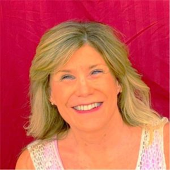 A woman with shoulder-length blonde hair, smiling warmly at the camera. She is wearing a light-colored, sleeveless top. The background is a solid, deep red color. The lighting is bright, giving the image a cheerful and vibrant feel.